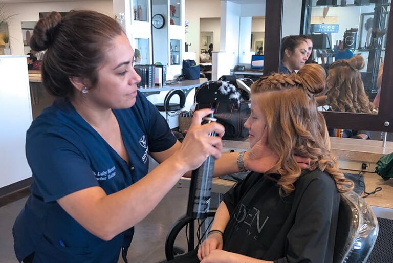 Hairdresser styling client's hair with spray in a salon setting.