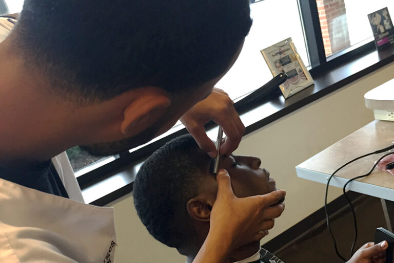 Barber precision trimming a client's hairline in a modern barbershop setting.