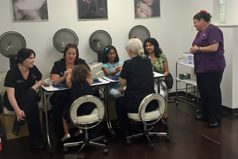Group of people engaged in a nail care session at a salon, with stylists and clients interacting.