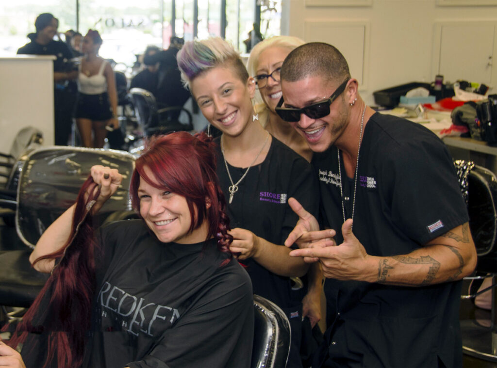 Smiling hairdressers styling client's red hair at a busy salon, showcasing creativity and teamwork.