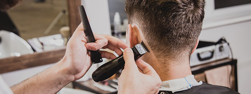 Barber using clippers for precise haircut on man's neck at barbershop.
