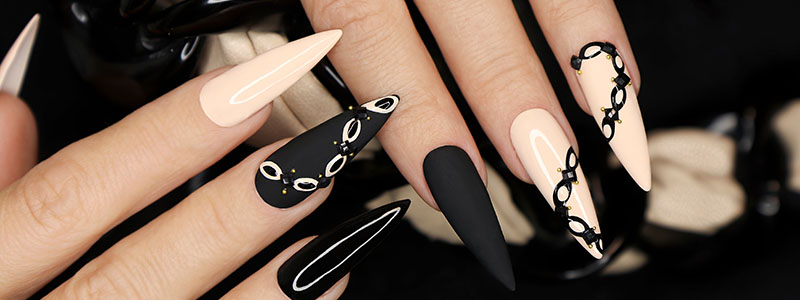 Stiletto nails with chic black and beige manicure, featuring intricate designs and glossy finish.