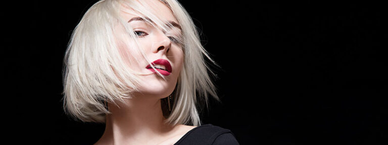 Stylish woman with platinum blonde bob hair and red lips on black background, showcasing modern beauty and fashion.