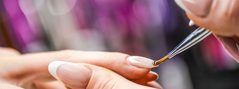 Manicure process: Applying nail polish on a woman's nails with precise brush strokes at a beauty salon.